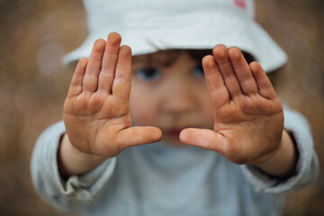 A little girl showing hear open dirty hands with her face blurred at the background 