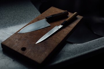 Japanese knives are lying on a cutting board on a kitchen counter under dramatic window light