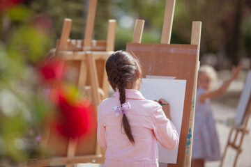 The girl draws in the park on an easel, plein air. Child learns to draw in nature
