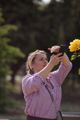 Beautiful girl takes a picture of a yellow rose on a smartphone