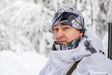 Portrait of a male hunter in a winter forest with a gun in a camouflage white suit. The concept of winter hunting.