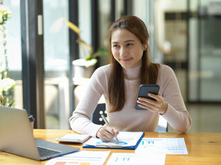 Female worker holding a smartphone while working on her paperwork