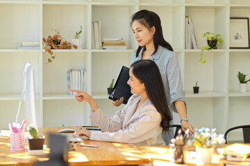 Female manager briefing and checking her assistant's work on pc desktop