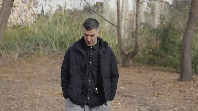 A man hangs his head, contemplating life as he walks alone through a secluded nature trail. Medium shot in slow motion.