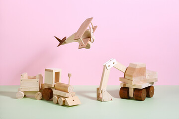 wooden toy airplane, train, and excavator on the pink and green pastel background