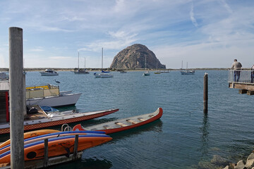 Morro Rock, which is an ancient volcanic plug, is shown along Californias Central Coast, with boats of the Morro Bay harbor in the foreground, during an afternoon day.