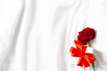 Holiday card top view red rose and box with gift on white bed. Valentine background. Happy Mother's day. Happy women's day. Happy birthday. Good morning. Marriage proposal