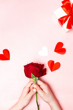 Holiday card top view: child's hands holding a red rose, box with gift, paper hearts. Valentine background. Happy Mother's day. Happy women's day. Preparation for the holiday