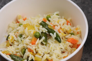 rice with vegetables in a cardboard plate macro photo

