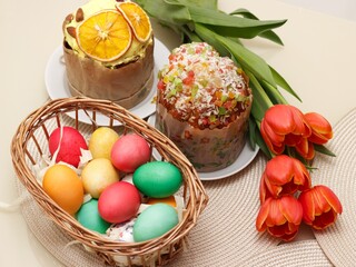Easter cakes and colored eggs in a wicker basket on the festive table.  next to flowers.