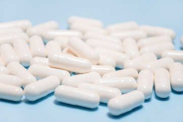Selective focus and soft focus on background of white tablets or capsules lie on a light blue background, side view. Pharmaceutical, Covid-19 or coronavirus