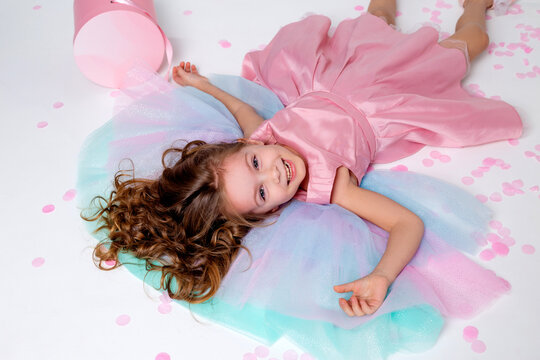 beautiful little girl in a chic pink dress lies on the floor strewn with confetti. top view. fashion and style. child celebrates his birthday. photo in the studio. space for text. High quality photo