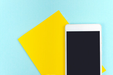 Yellow a piece of paper with empty screen mobile phone on blue background.