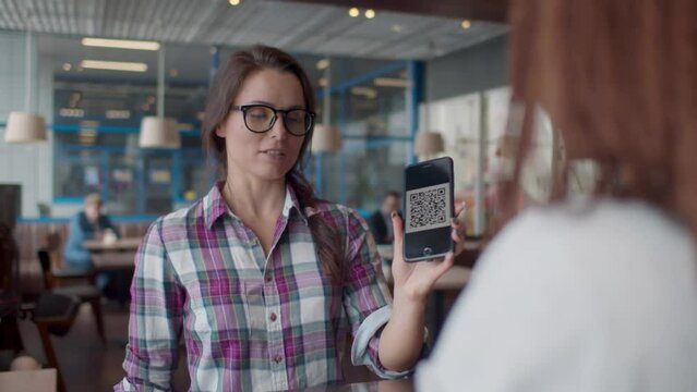 Smiling woman showing qr-code on smartphone to waitress in coffee shop. Realtime