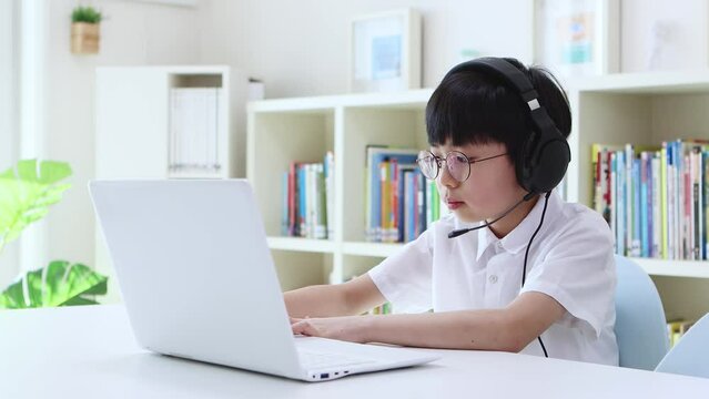 Cute and adorable young student wearing wireless headphones and concentrating on online class with laptop at home