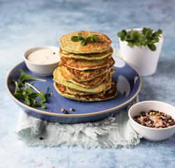 Stack of broccoli or spinach pancakes with yoghurt or cream sour dressing and microgreen, blue background. Vegetarian fritters. Healthy food.