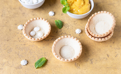 Empty shortbread tartlets, lemon curd, mini meringues and mint. Process making dessert.