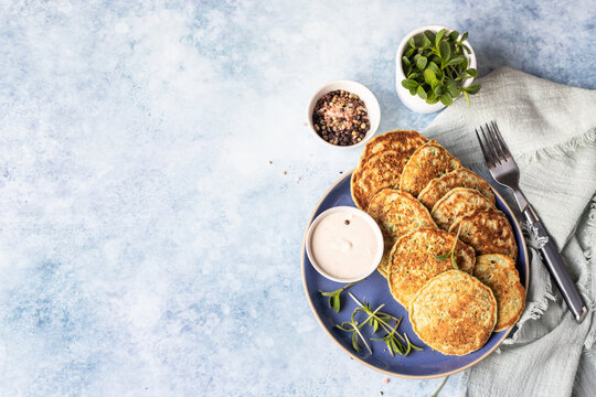 Vegetable fritters or pancakes made of zucchini, broccoli or spinach on plate with microgreen and dip, blue background. Healthy vegetarian food. Top view.