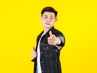 Portrait studio shot Asian young handsome male hipster model wearing casual street denim jacket jeans standing look at camera posing on yellow background.