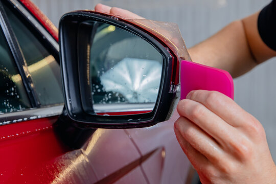 Closeup Installs vinyl film for protect paint body side mirrors red car