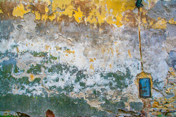 An old wall with partially collapsed paint and an unusual multicolored texture and little door. Natural background with layers of different colors.