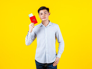 Portrait studio shot of Asian young male traveler model in casual outfit standing posing smiling look at camera holding showing red Singapore passport and boarding pass ticket on yellow background