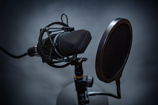 Close-up of a professional microphone with a pop filter in front of it. Desktop microphone for recording podcasts, songs and streaming on a stand against a dark background
