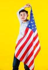 Portrait studio shot of millennial Asian young handsome male US citizen businessman model in casual outfit standing holding big United States of America USA national flag sheet on yellow background