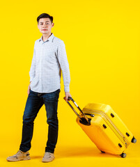 Portrait studio shot of millennial Asian young handsome male businessman traveler model in casual outfit standing smiling holding big trolley luggage traveling for business trip on yellow background