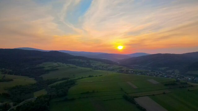 Aerial shot over the fields and meadows of a mountain valley towards the sunset with stunning cloudscape