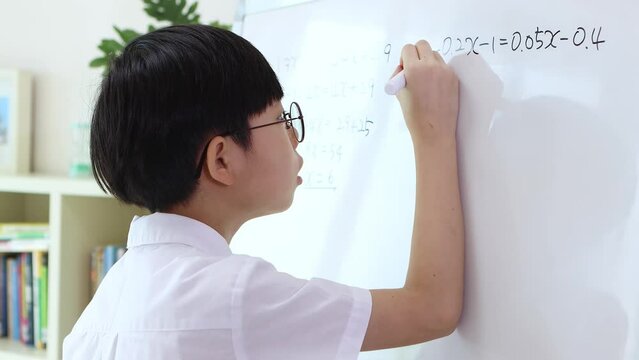Smart and cute boy concentrating on his studies while working hard on the blackboard solving math problems