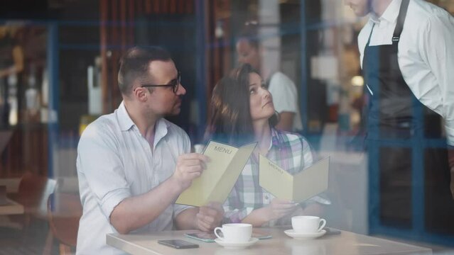 View through window of happy couple with menu order food in restaurant. Realtime