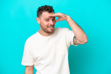 Young Brazilian man isolated on blue background looking far away with hand to look something