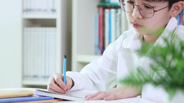 A child who is tired of boring school homework and studying is studying hard by taking notes in a notebook even though he is tired.