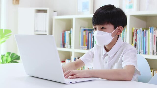 Child in mask taking online class with laptop, exchanging messages and talking