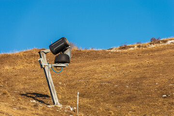 Snow cannon or snowmaking system in winter on a brown meadow, ski slope, without snow due to the...