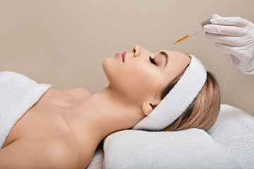 Beautician applies serum to woman's face with pipette, side view. Facial skin care with treatment cosmetic oil and serum