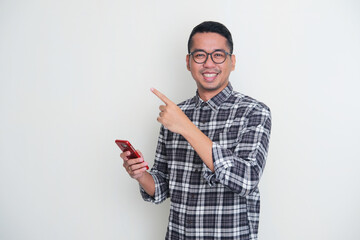 Adult Asian man pointing to the right and showing happy expression when holding his mobile phone