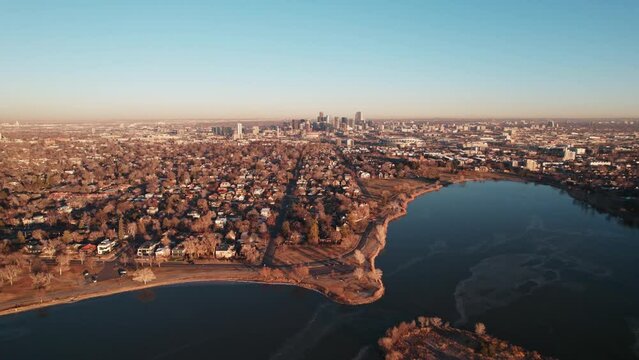 Sloan Lake Denver Colorado USA. Drone Aerial Footage Flying Over Deep Blue Lake Showing Downtown Skyline And Cityscape Seen From Sloan Lake During Warm Glowing Golden Hour Sunset.