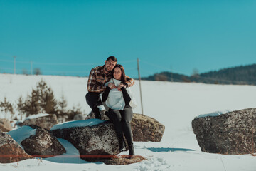 Lovely romantic couple sitting hugged and laugh happily on a rocks against frozen space. Selective focus.