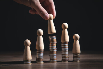 Male hand showing wooden human figure on coins stack.