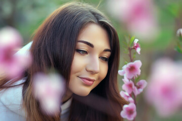 Fototapeta premium Smiling beautiful girl standing near a peach tree during sunset. Happy face. Spring time.