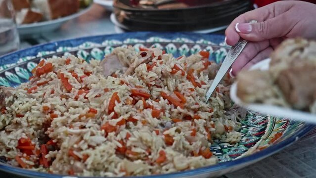 Woman puts pilaf in her plate. Eating outside the house.