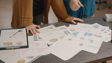 Close up of colleagues checking papers with data rate charts on table. People using information files to plan business project and presentation, working on startup organization development