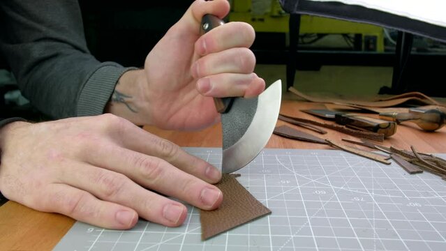 Close up hands tanner cuts special halberd cutting knife leather piece in workshop. Craft production.