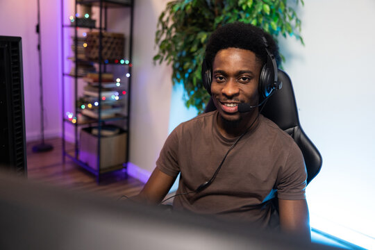 Portrait of a man Africa America sitting on a comfortable chair with a headset in a colorful led lit room, a professional gamer is hosting a live stream for pc game fans