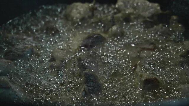 Close up view of meat being fried in a big cauldron. Cooking pilaf