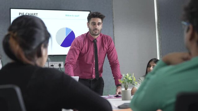 Young indian businessman corporate leader coach speaker give flip chart workshop presentation explaining strategy teaching multiethnic staff consult diverse team at office meeting training concept.