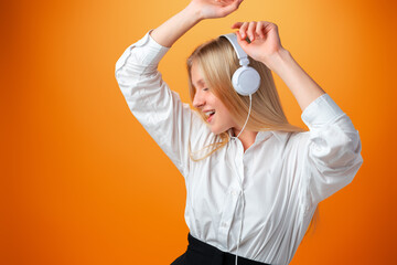 Portrait of modern happy teen school girl with headphones on orange background