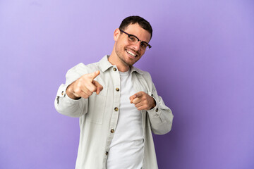 Brazilian man over isolated purple background surprised and pointing front